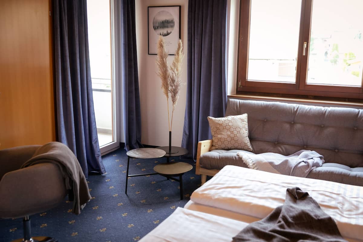 Ett hotellrum med en säng, en soffa, en stol, ett litet bord och ett fönster med gardiner.