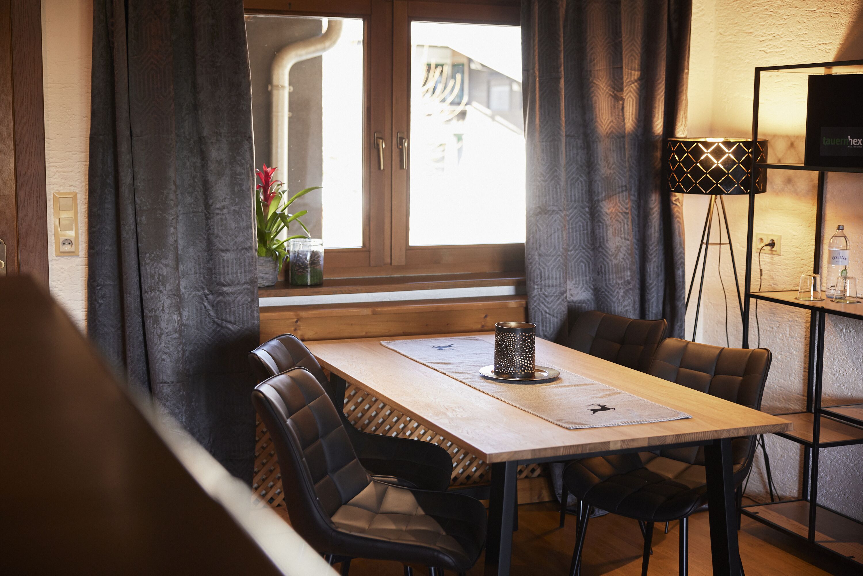 Un comedor con una mesa de madera, sillas tapizadas negras, una planta pequeña en maceta y una lámpara de pie.