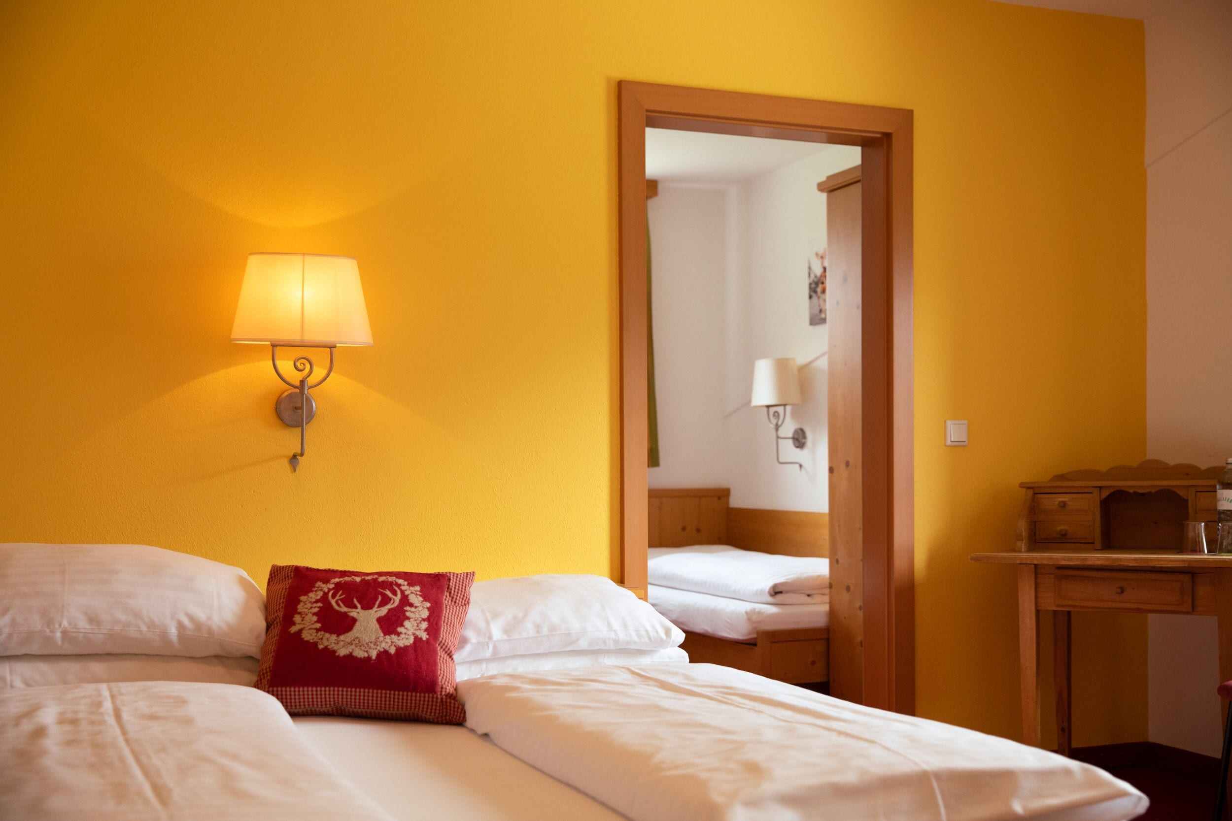 A hotel room with two beds, a wooden desk, a mirror, and a wall-mounted lamp.