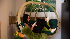 Una persona sentada en una silla colgante circular con un reposapiés mullido, sosteniendo un teléfono inteligente.