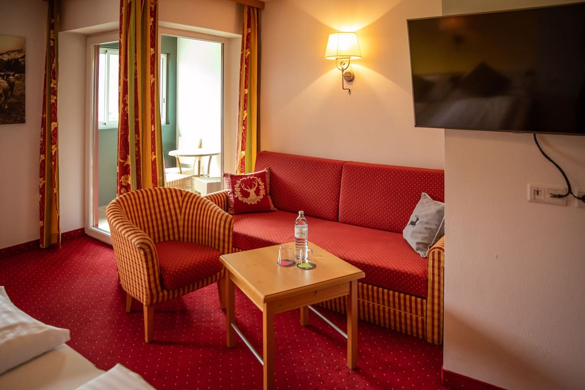 Ett hotellrum med en röd soffa, en randig fåtölj och ett litet träbord med en flaska och glas.