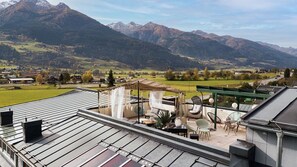 Eine Dachterrasse mit Bergblick, Außenbestuhlung und einer Pergola.
