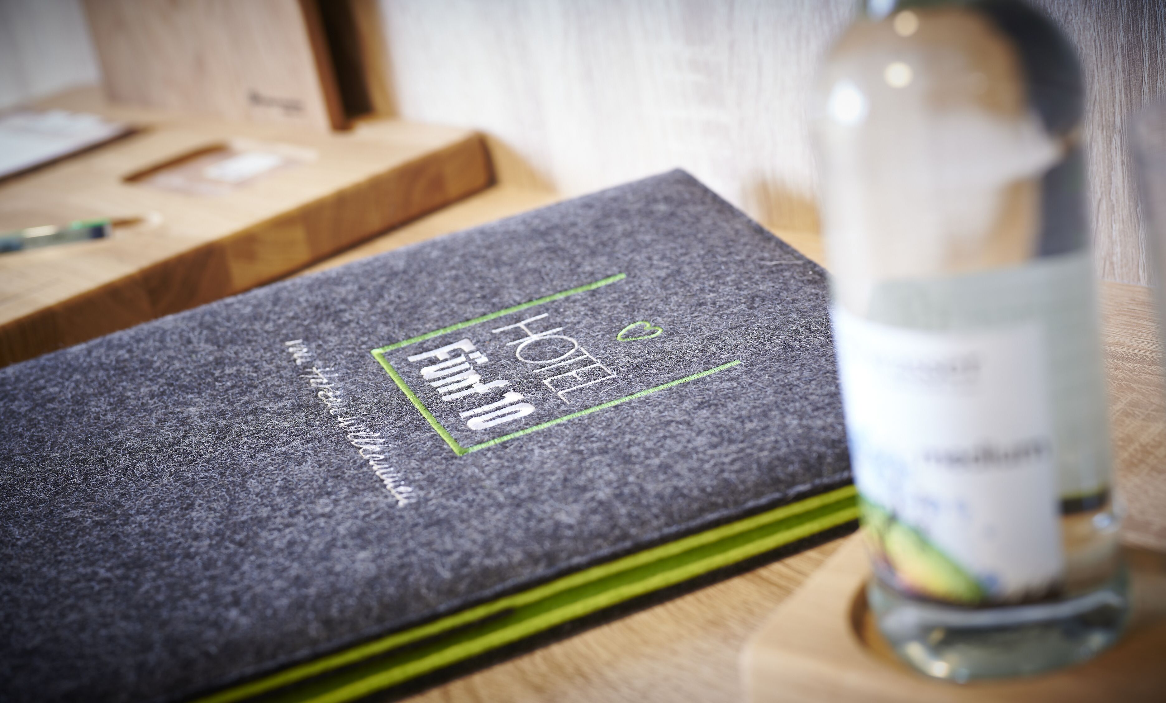 Een donkergrijze hotelkamer met een bed, een houten nachtkastje en een fles water.