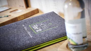 Een donkergrijze hotelkamer met een bed, een houten nachtkastje en een fles water.