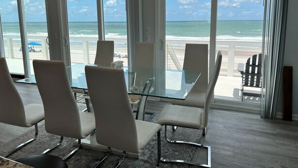Un salón de conferencias con una mesa y sillas de vidrio, y ventanas amplias con vista a la playa.
