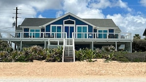 Una casa frente a la playa con un porche cubierto, una escalera que lleva a la entrada y vistas al océano.