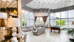A spacious living area with a pool table, comfortable seating, and large windows offering a view of greenery. - Happy Days Hotel (Rhodes)