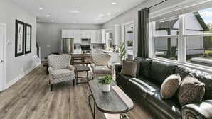 Eine moderne Küche mit weißen Schränken, ein Essbereich mit gemusterten Stühlen und ein Ledersofa mit dekorativen Kissen.
