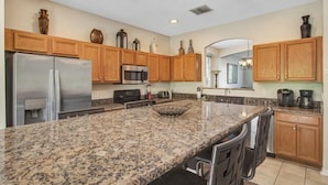 A kitchen with granite countertops, wooden cabinets, stainless steel appliances, and a central island with bar stools.