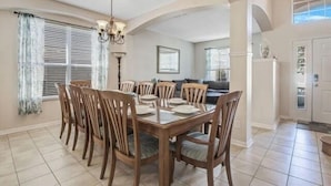 A dining area with a wooden table and chairs, a chandelier, and a view of a living room.