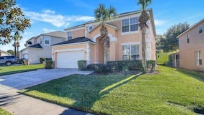 A two-story house with a garage, a well-maintained lawn, and a palm tree.