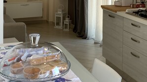 Une cuisine moderne avec un coin repas, un téléviseur à écran plat fixé au mur et un espace dédié au petit-déjeuner avec des viennoiseries.
