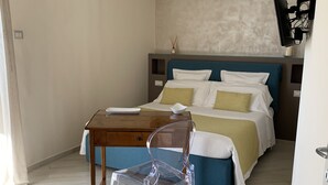 Une chambre à coucher avec un lit, une table en bois, une chaise en plastique transparent et un téléviseur fixé au mur.