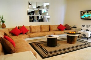 Un salon avec un canapé marron, des coussins rouges, une table basse et un téléviseur fixé au mur.