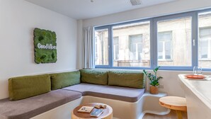 A modern living room with a sectional sofa, a wooden coffee table, and a view of the street through large windows. - LOFUS bio-suites (Athens)