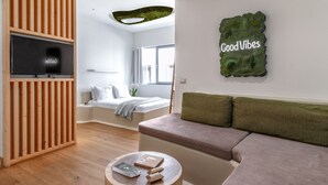 A modern living room with a wooden slat wall, a flat-screen TV, a green wall art piece, a sofa, and a round wooden coffee table. - LOFUS bio-suites (Athens)
