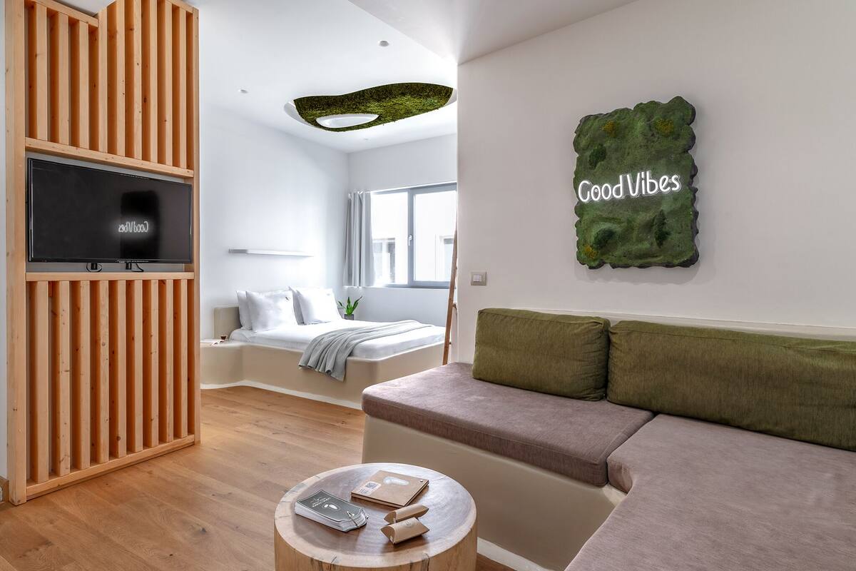 A modern living room with a wooden slat wall, a flat-screen TV, a green wall art piece, a sofa, and a round wooden coffee table.