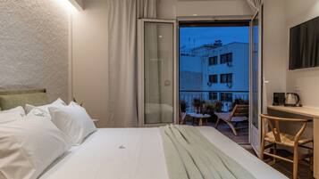 A hotel room with a bed, a desk, a chair, and a balcony with a view of the building.