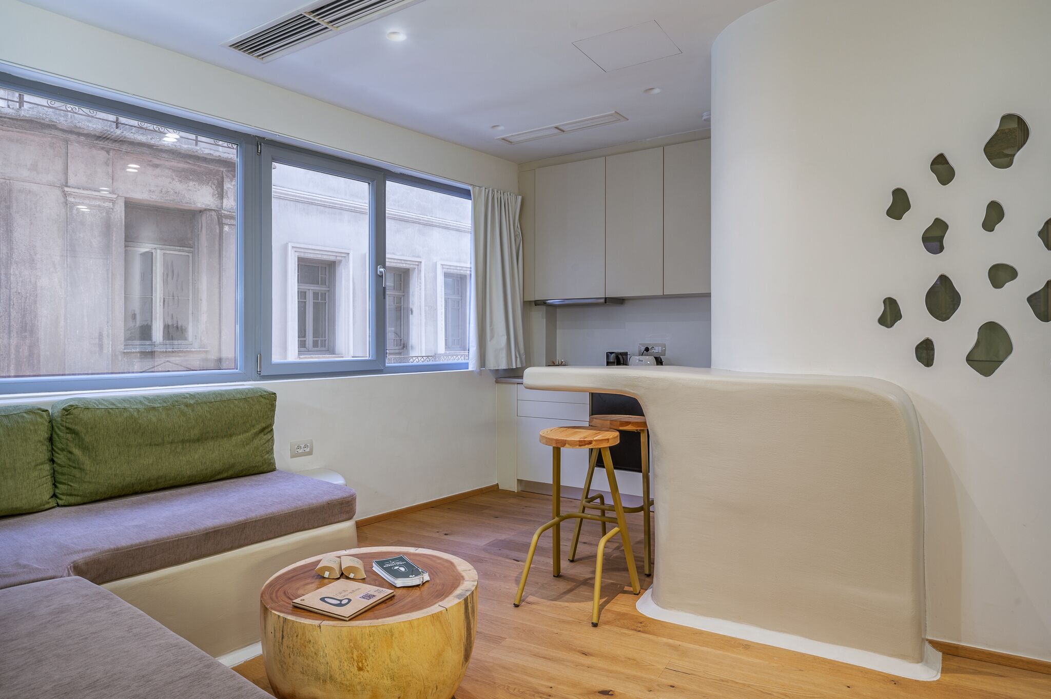 A compact living space with a sofa, a small round table, a stool, and a kitchenette area.