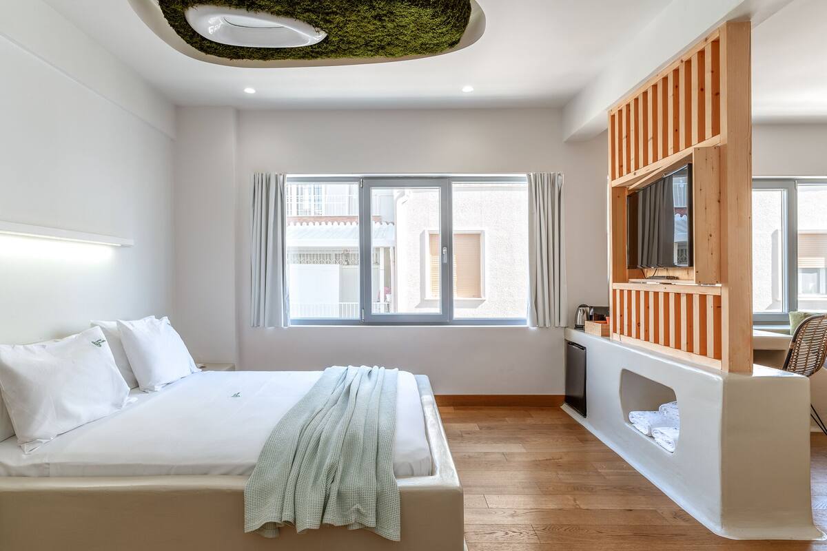 A modern bedroom with a bed, a TV, a small seating area, and a window with curtains.