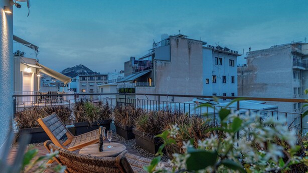 A rooftop terrace with wicker furniture, a table with a bottle and glass, and potted plants. - LOFUS bio-suites (Athens)