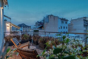 A rooftop terrace with wicker furniture, a table with a bottle and glass, and potted plants. - LOFUS bio-suites (Athens)