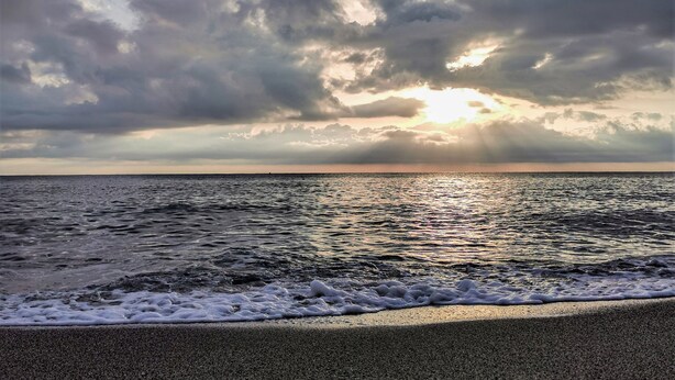 A beach with waves and a cloudy sky.