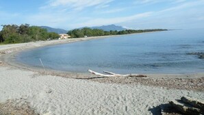 A beach with a curved shoreline, a clear sky, and distant mountains.