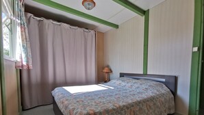 A bedroom with a bed, a window with curtains, a lamp, and a green wall.