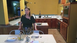 A dining area with a table set for two, a kitchen in the background, and a person standing by the table. - Casa La Reforma TRINIDAD (Trinidad)