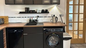 Una cocina funcional con lavavajillas, lavadora y cafetera sobre la encimera.