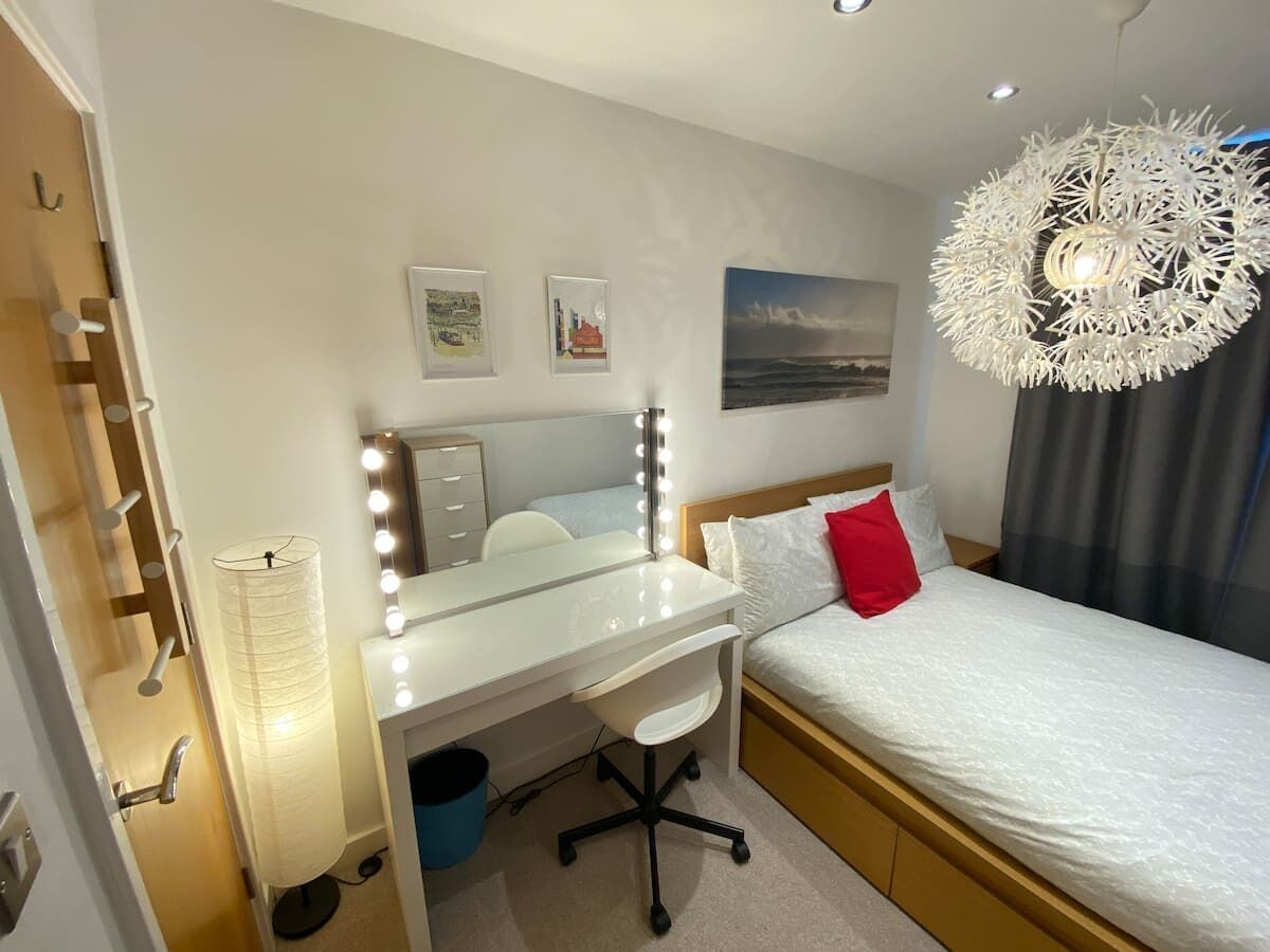 Een slaapkamer met een bed, een bureau met spiegel en een wandlamp.