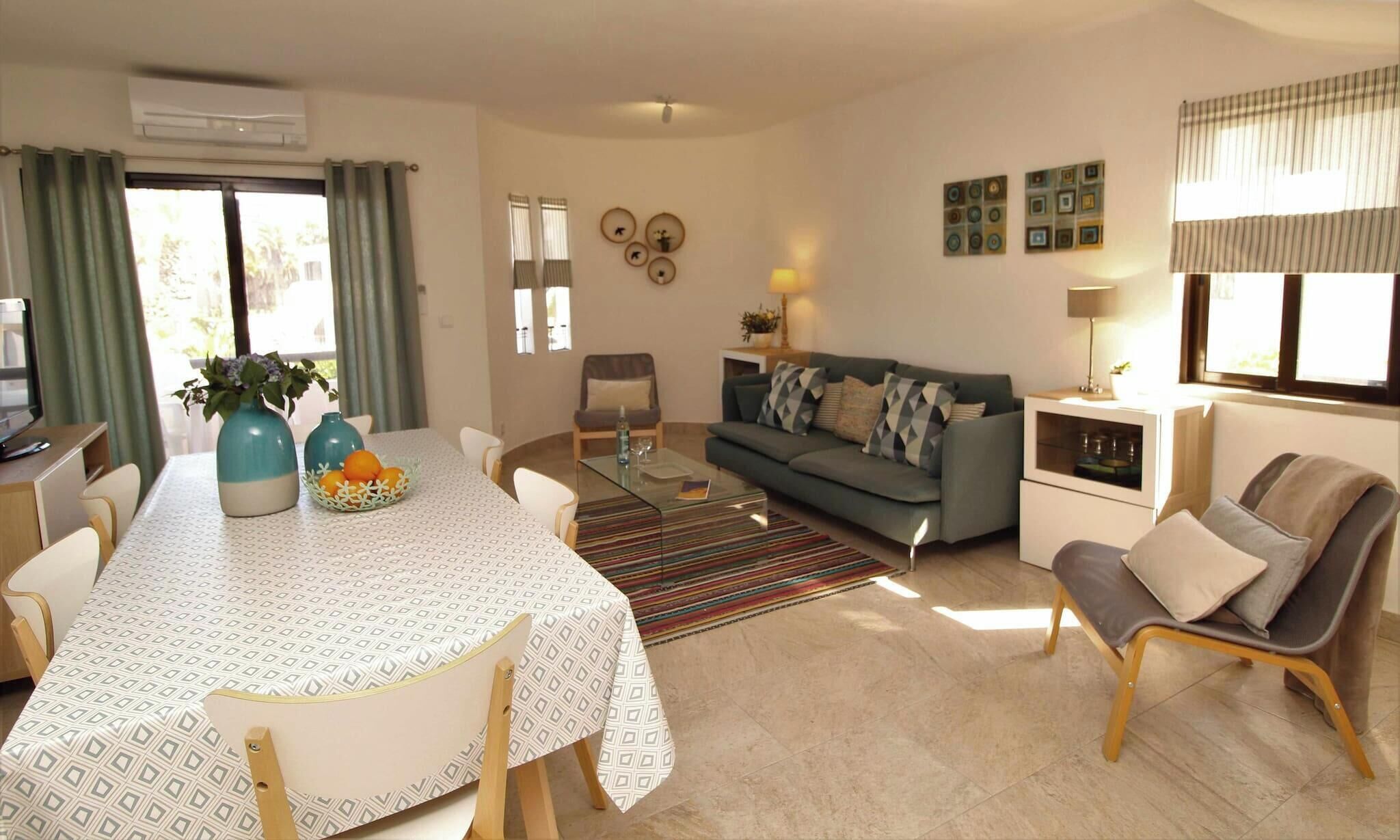 A modern living room with a dining table, sofa, and chairs. There is a window with curtains, a lamp, and wall decorations.