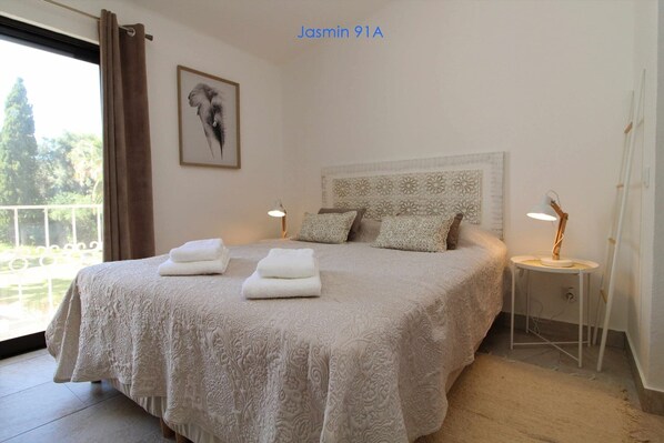 A neatly made bed with a patterned bedspread, two pillows, and folded towels on the side. There is a framed artwork on the wall and a small table with a lamp beside the bed. - 2 Bedroom Duplex Apartment with Swimming pool at São Rafael Beach - Albufeira (Albufeira)