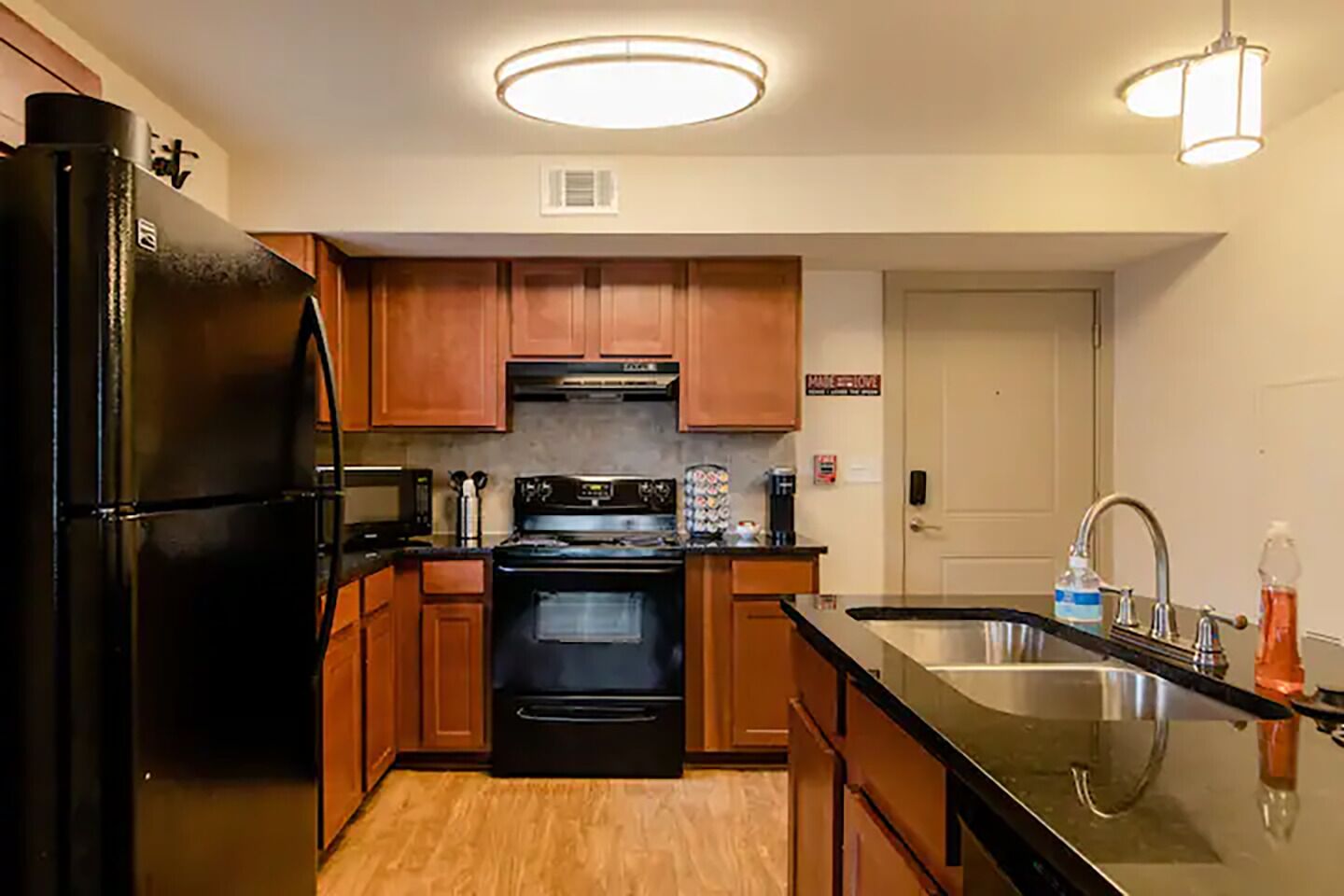 A compact kitchen with wooden cabinets, a black refrigerator, a stove, and a sink.