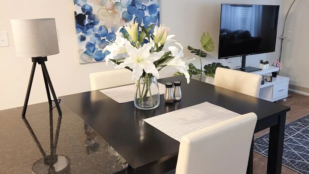 A dining area with a black table, white chairs, a vase with flowers, a painting on the wall, and a TV on a stand. - 10 minute Walk GA Aquarium and other Major Attractions (Atlanta)