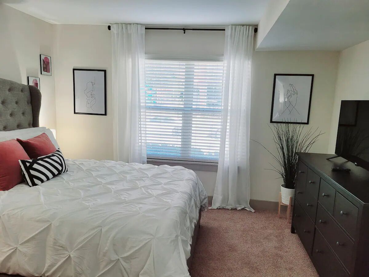 A bedroom with a bed, a dresser, a TV, and a window with blinds.