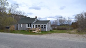 A two-story house with a porch, a small attached garage, and a wooden staircase leading to the front door. - Quiet and Cozy Seaside Cottage with Amazing Sunsets (Steuben)