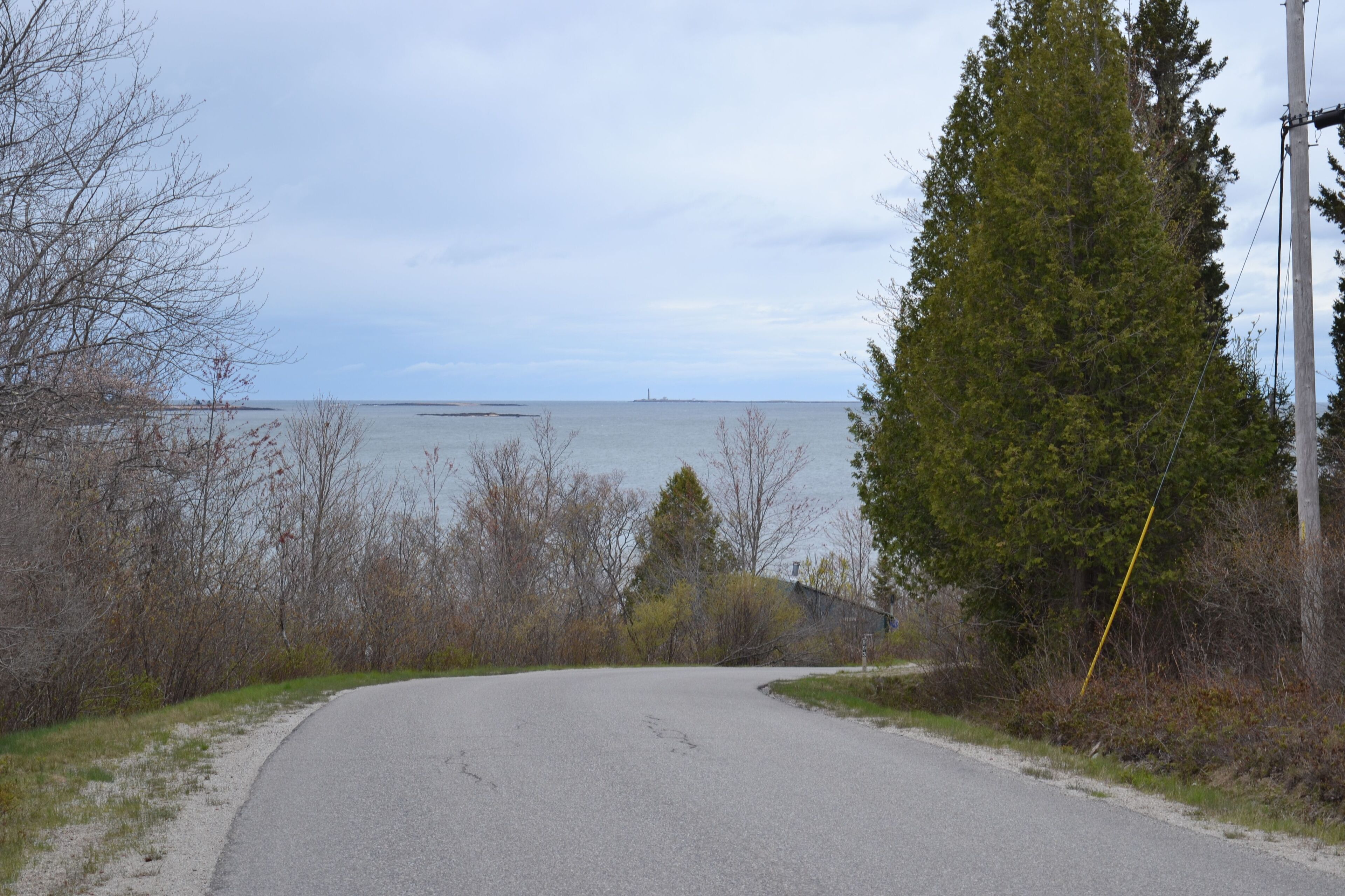 A coastal road with a view of the sea and a lighthouse in the distance.