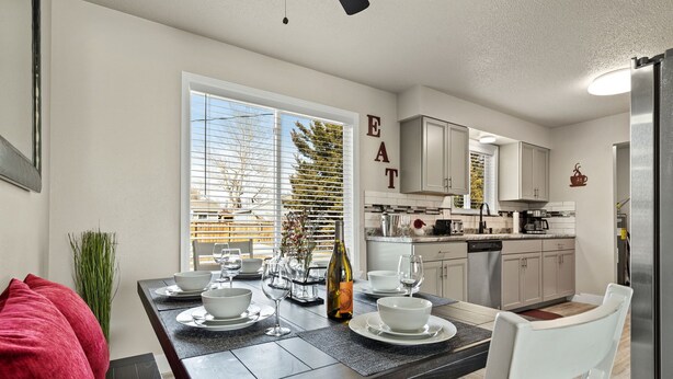 A modern kitchen with a dining area, featuring a large window, white cabinets, and a "EAT" sign on the wall. - Relaxing Hot Tub and Fire Pit! Great for Families or Business - Perfect Location (Loveland)