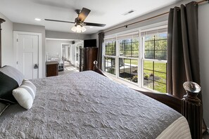 Un dormitorio con una cama grande, un ventilador de techo y vista a un patio trasero a través de una puerta corrediza de vidrio.