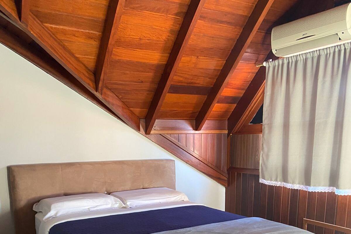 Un dormitorio con cama, vigas de madera en el techo y una ventana con cortinas.