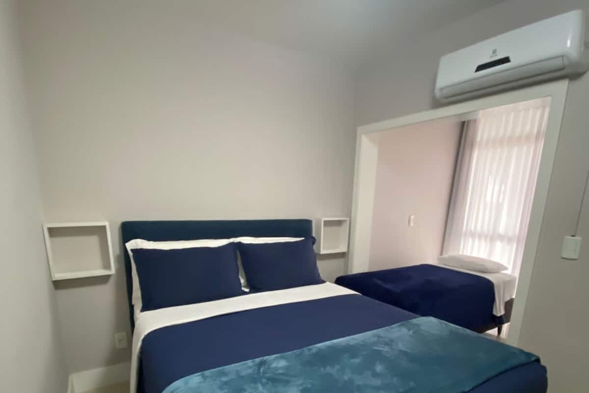 Un dormitorio con cama, mesita de noche, equipo de aire acondicionado y ventana con cortinas.