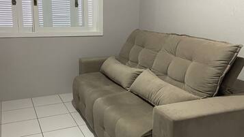 Ein beiges Sofa in einem Raum mit weiß gefliestem Boden und einem Fenster mit heruntergelassenen Jalousien.