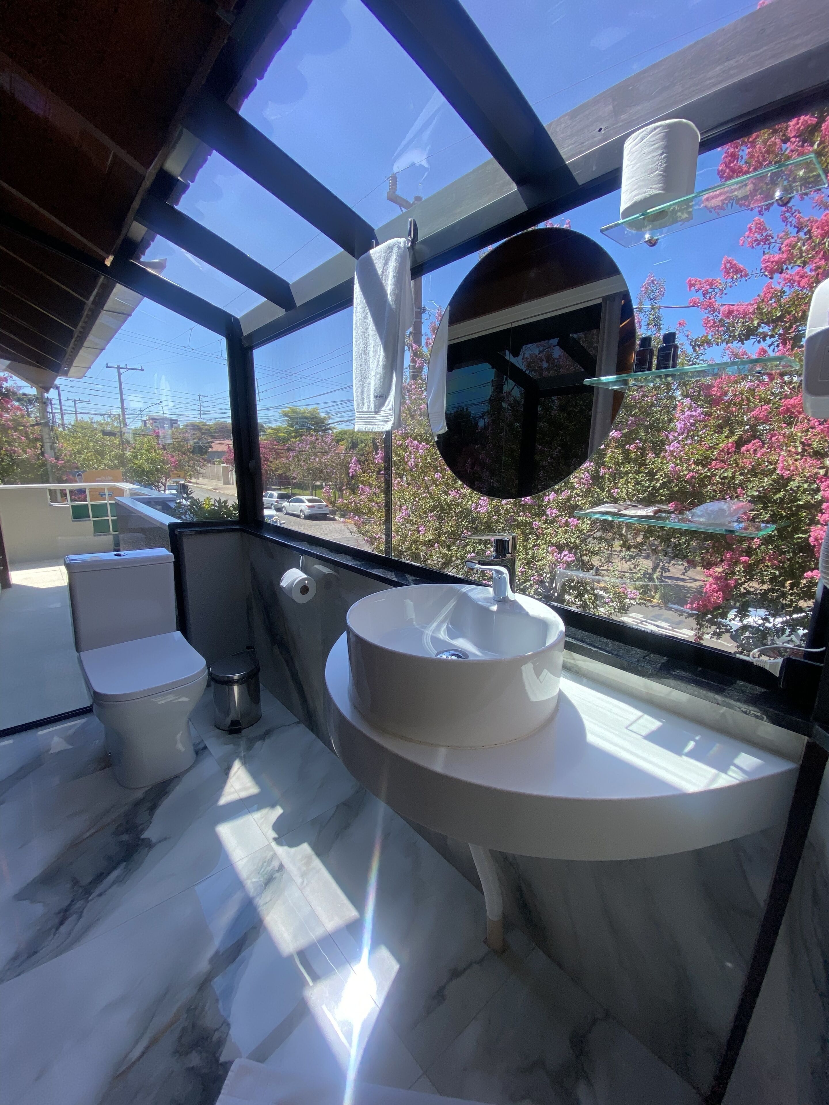 A modern bathroom with a large window, a round mirror, and a white sink.
