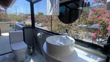 A modern bathroom with a large window, a round mirror, and a white sink.