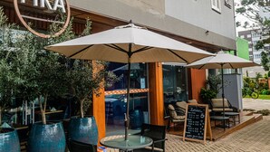 An outdoor seating area with tables and umbrellas, a sign reading "FIKA", and a menu board outside a building. - FIKA Residence (Dois Irmaos)