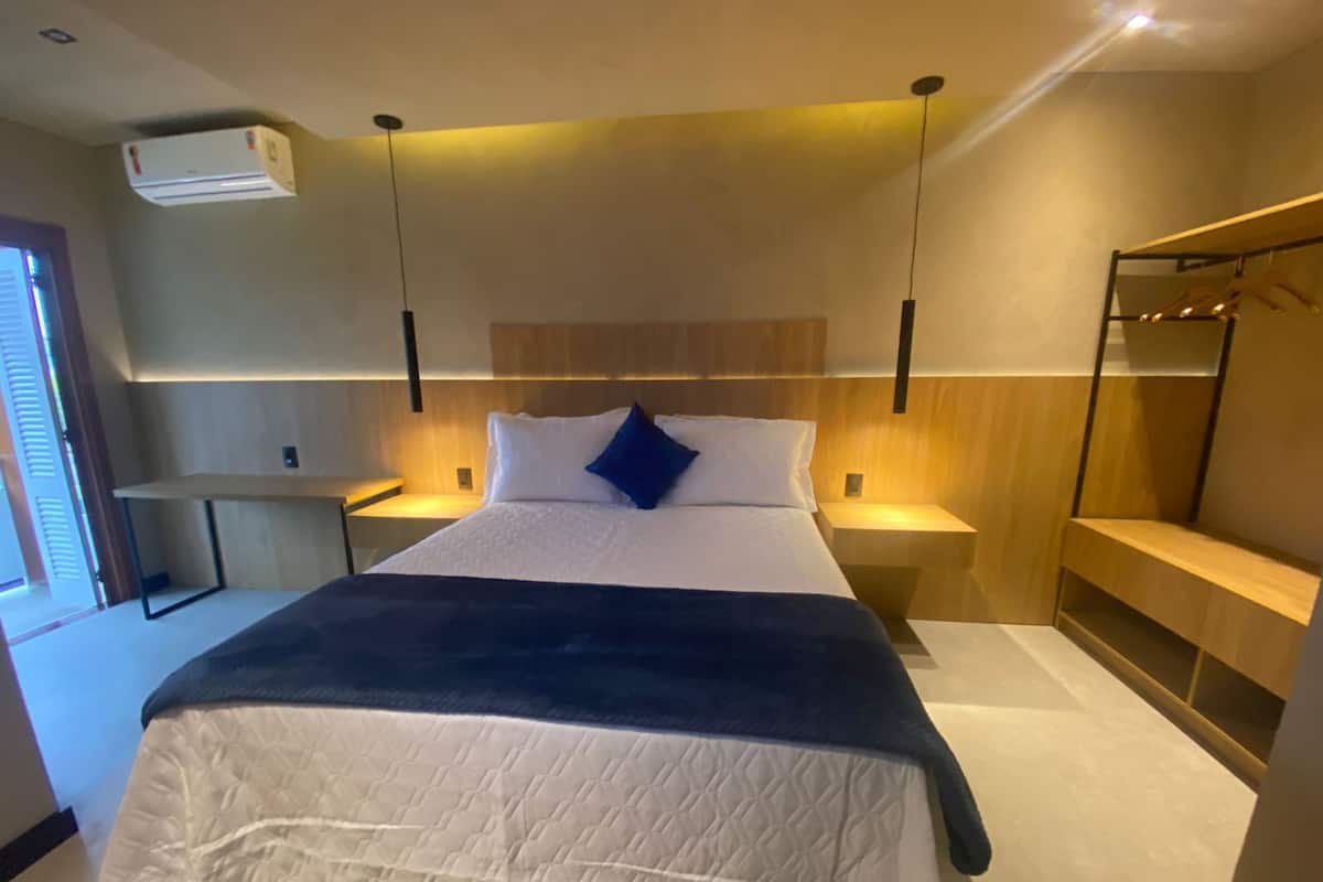 Una habitación de hotel moderna con una cama grande, mesitas de noche, un armario y un equipo de aire acondicionado.
