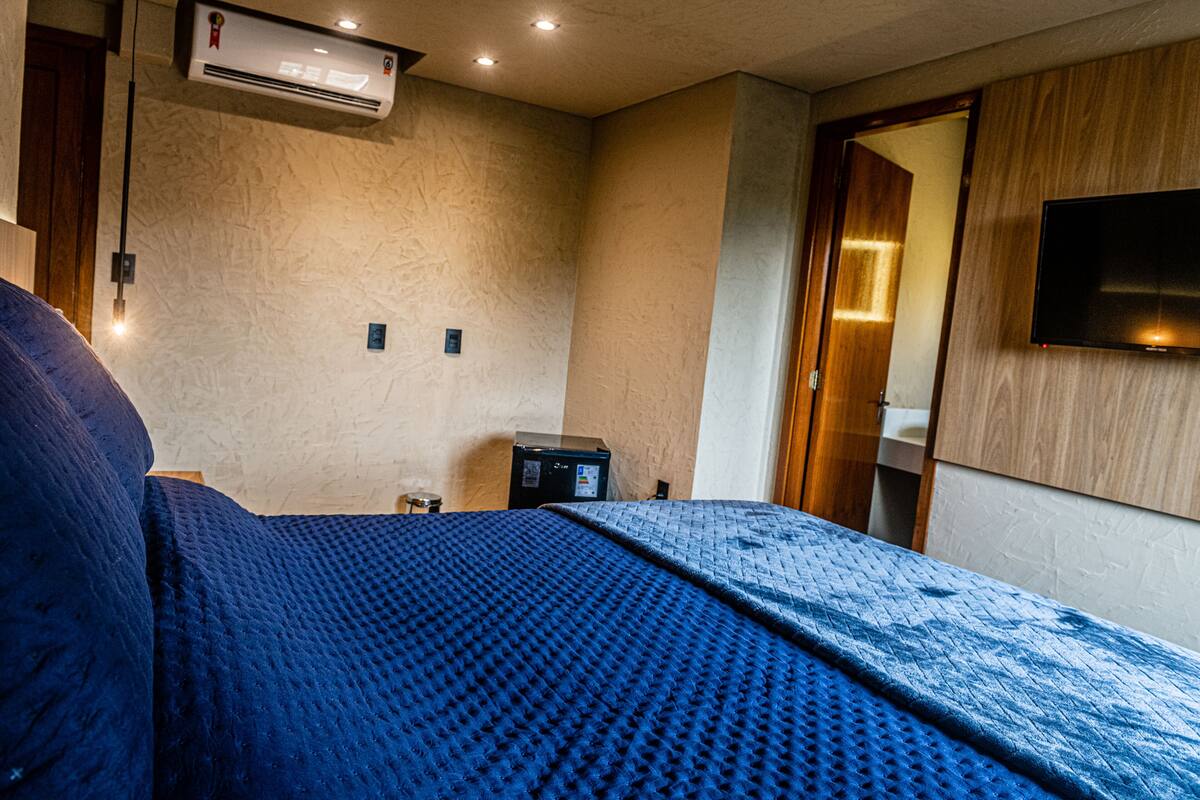Un dormitorio con una cama, un televisor montado en la pared y una mesita de noche.