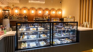 A bakery display case with various pastries and desserts, a bar area with bottles and glasses, and a wall-mounted air conditioner. - FIKA Residence (Dois Irmaos)